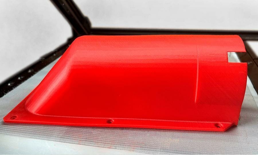 Großes, hohl gedrucktes abgerundetes 3D Bauteil aus rotem Kunststoff, an den Rändern sind Schraublöcher, an der offenen Seite ist eine rechteckige Aussparung. Das Objekt ist auf dem Belt des One Pro von iFactory3D platziert.