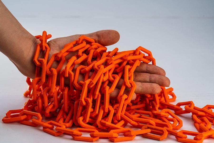 Eine Hand greift in eine lange, einfach konstruierte Kette mit großen Kettengliedern, gedruckt mit orangem iFactory3D PETG Filament.