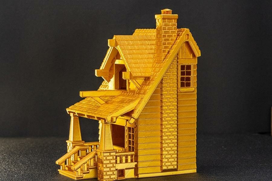 Gold glänzendes 3D gedrucktes Vogelhäuschen mit Veranda, Schonstein und Obergeschoss.