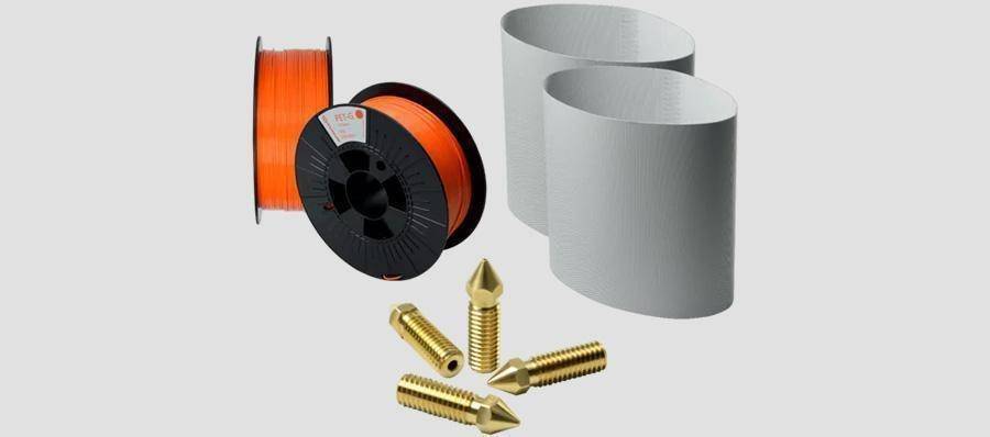The care package shown consists of two orange filament rolls of 1kg each, two assembly line belts and four replacement nozzles.