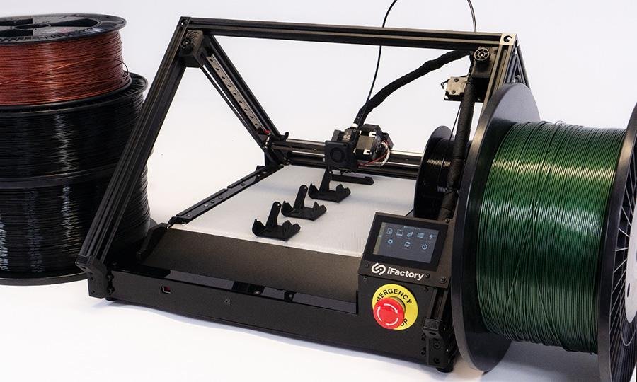 Studio shot One Pro, with large filament spools on both sides; there are 3 identical black technical printed parts on the belt, plus a semi-finished one directly on the print head