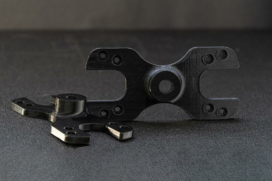 Zwei gedruckte x-förmige Bauteile mit zentralem Loch aus schwarzem PETG Filament Material