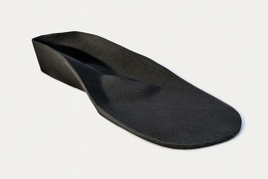 Black filament 3D printed insole that follows the organic shape of the foot, lying down and shown in half profile