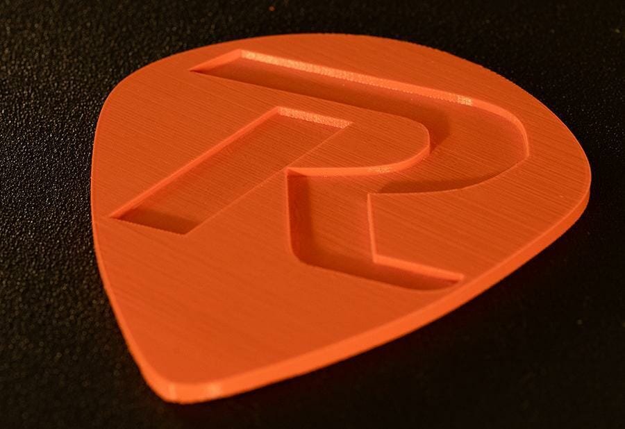 Print example of a plectrum with deep relief drawing of the letter R; made of orange iFactory3D PETG