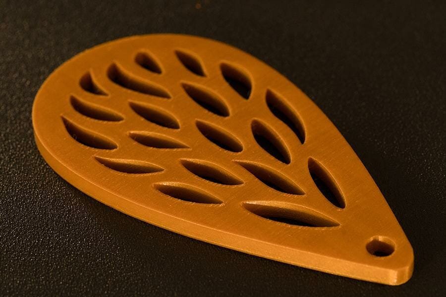 Gallery image of wing shaped object with elliptical hole pattern and screw hole at the top; 3D printed with gold PLA filament.