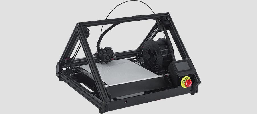 3D conveyor belt printer ONE PRO with pyramid-like structure, black frame and silver print bed; black filament spool in the construction space, which is located just behind the screen and emergency stop button