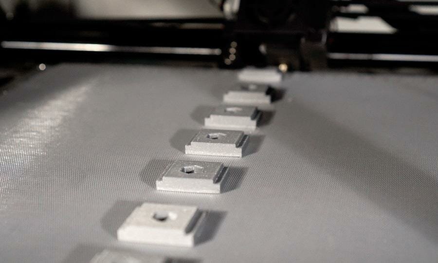 Nahaufnahme von Seriendruck kleiner silberner quadratischer Plättchen mit mittigem Schraubloch auf silbernem Belt des One Pro von iFactory3D