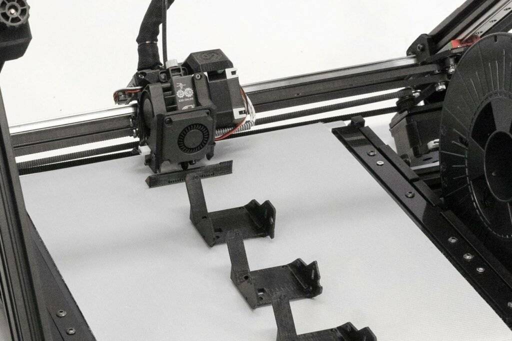 Der 3D-Fließbanddrucker One Pro von iFactory3D bei der Produktion einiger technischer Teile aus schwarzem PETG Material