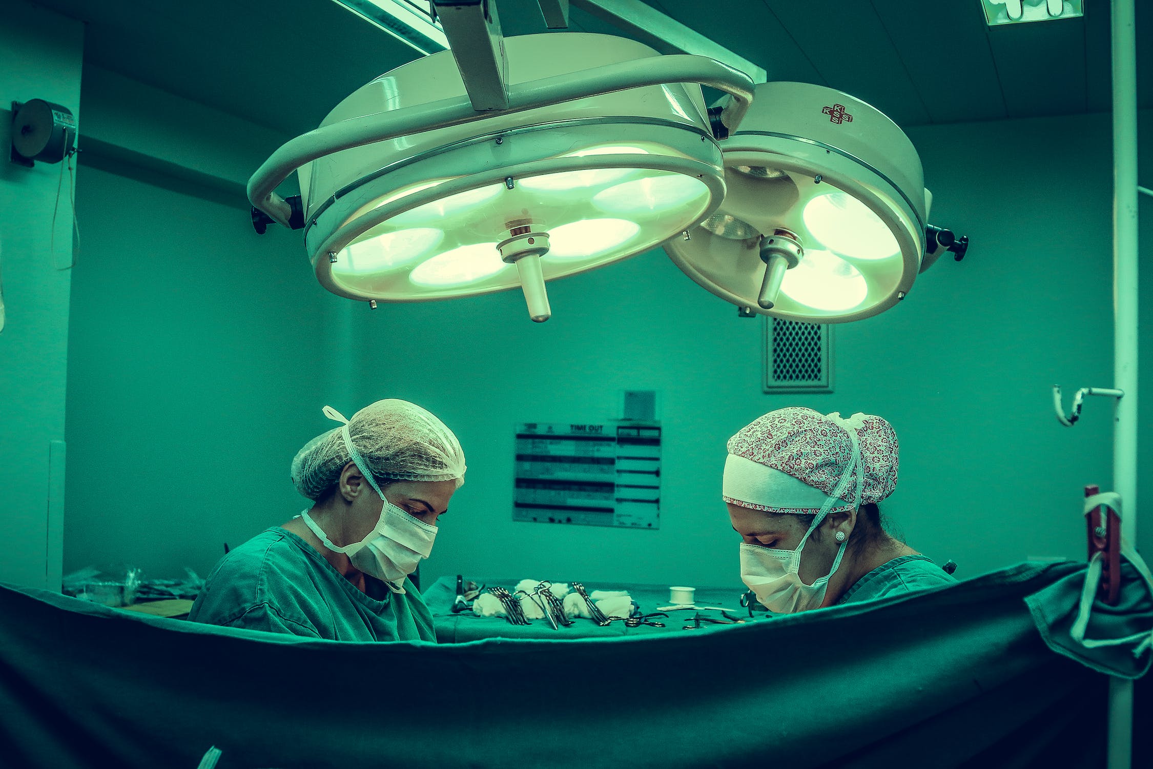 An operating room with two people wearing surgical hoods and face masks, in the background surgical instruments