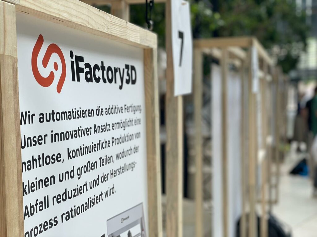 Schild von iFactory3D auf einer Messe inmitten einer grünen Kulisse mit natürlichen und nachhaltigen Materialien