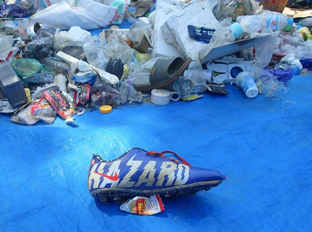 Ein Sportschuh mit der Aufschrift "Hazard" vor einem Abfallhaufen