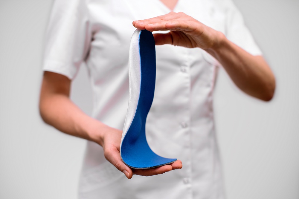 Person hält eine flexible orthopädische Einlage mit blauer Oberfläche in den Händen.